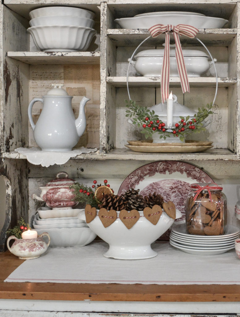 A chippy white cupboard filled with ironstone and red and white dishes for Christmas