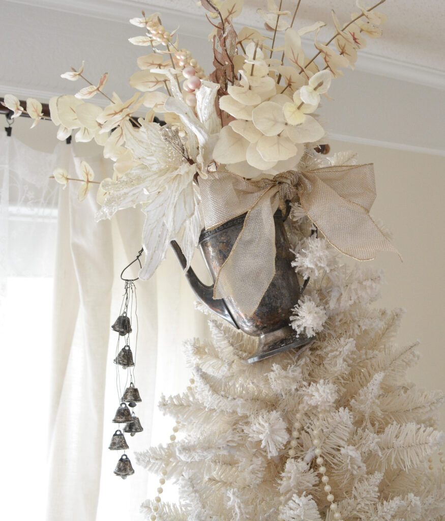 A Christmas tree topper made out of a silver teapot filled with flowers and pouring silver bells.