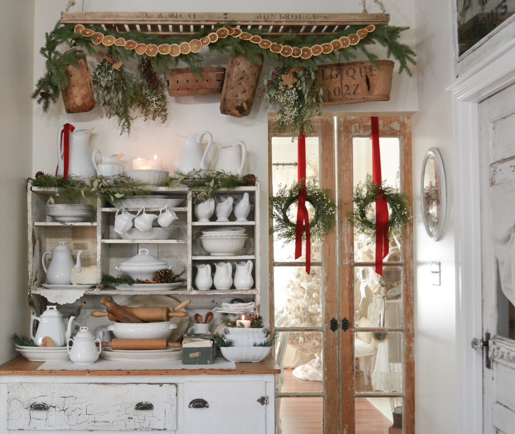 French dying rack with orange slice garland hangs over chippy cupboard filled with ironstone china.