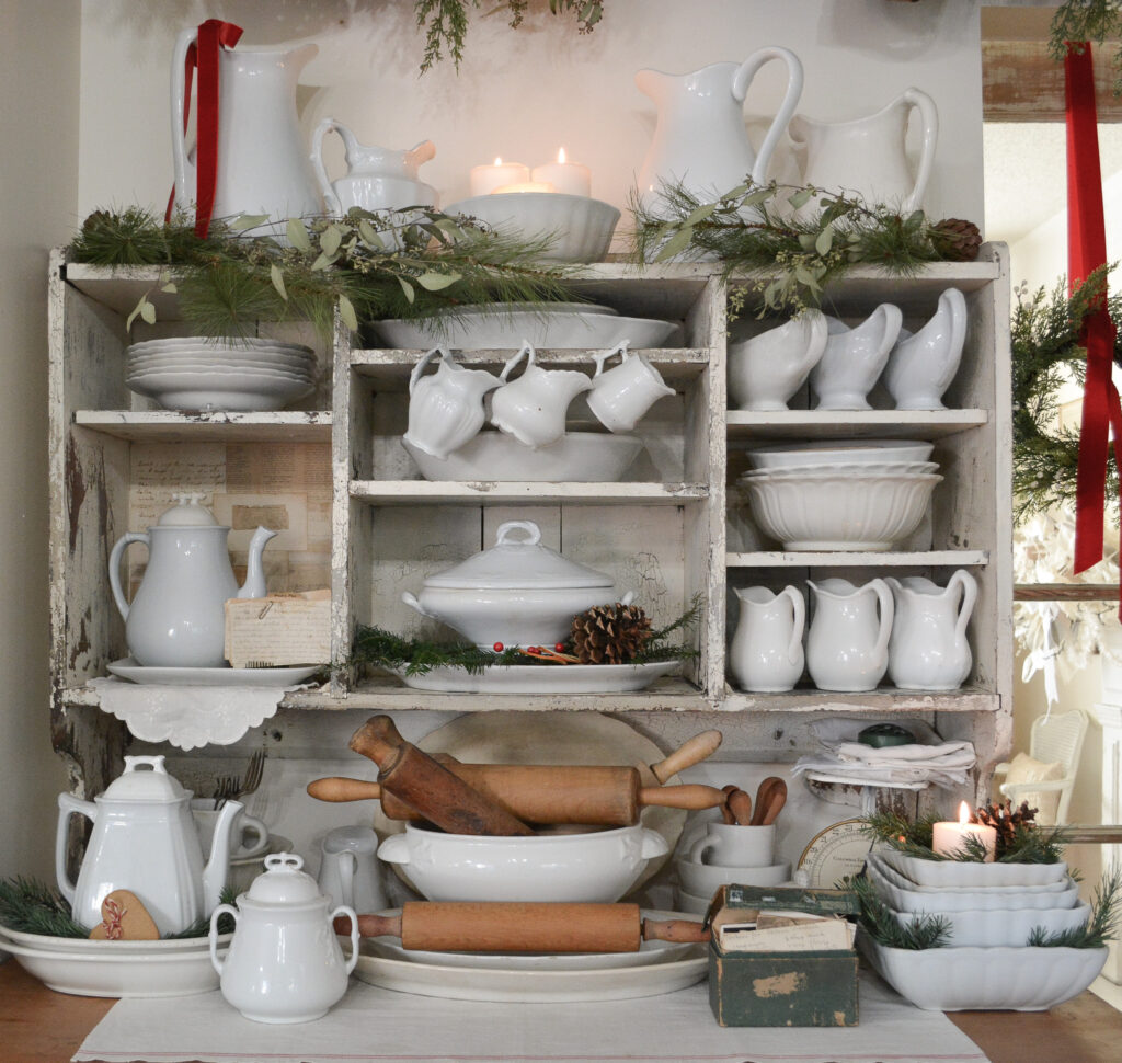A chippy white cupboard filled with antique ironstone and greenery for Christmas