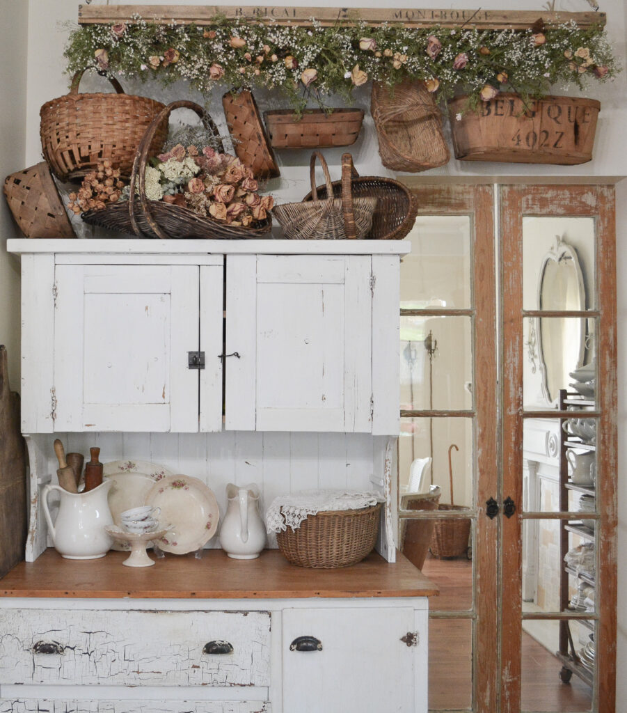 A country hutch with baskets and dried flowers on top
